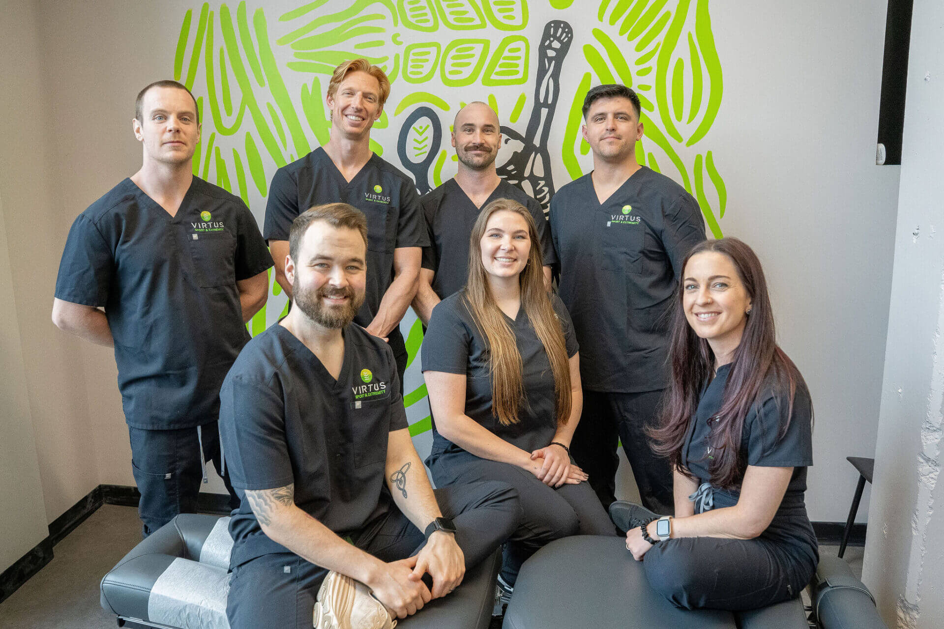 Virtus clinic team posing in front of a mural