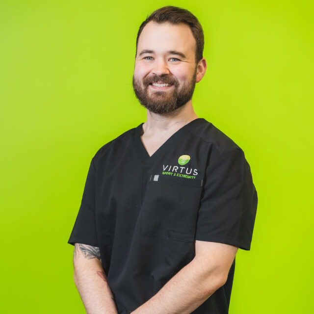 tristan-maxwell-2026 Dr. Tristan Maxwell smiling wearing black Virtus scrubs, professional portrait